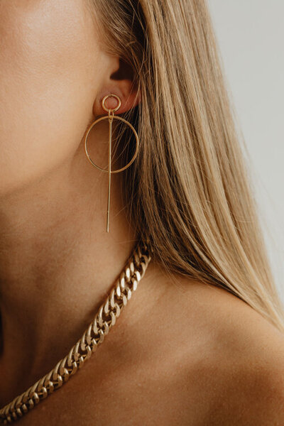 detail krku a části tváře ženy, na uchu má zlatou náušnici a na krku zlatý řetězový náhrdelník