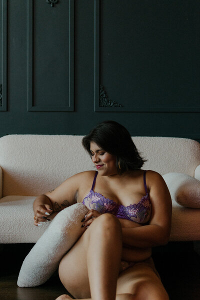 Studio boudoir session in Salem, Oregon with a woman sitting on the floor in a lingerie set, holding a pillow.