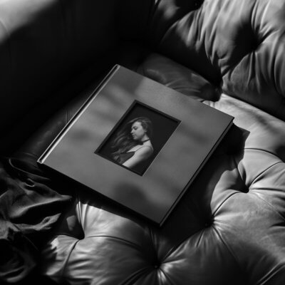 Opulent photo album with female portrait on its cover, laying on a luxury sofa