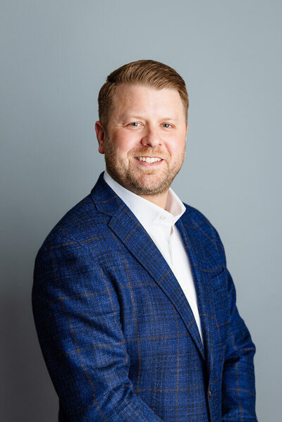 Man with beard in blue jacket looks at camera for his headshot session.