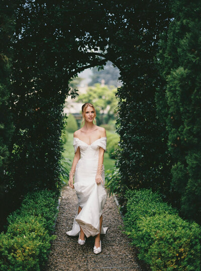 Photo of a bride in a flowing white dress walking through a hedge tunnel in the garden grounds of Villa Balbiano on Lake Como in Italy