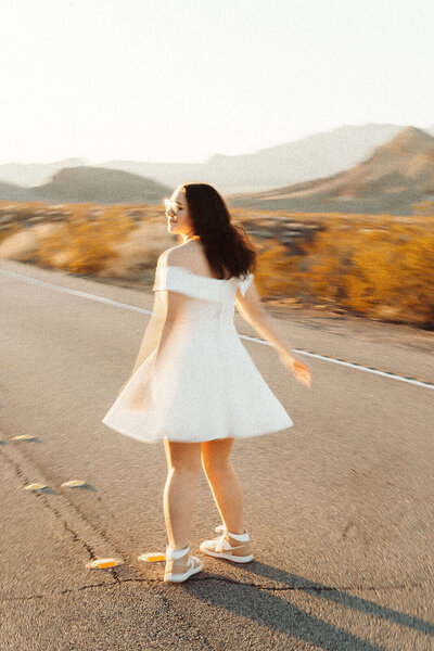 The girl in a white dress is twirling on the road in the middle of the desert