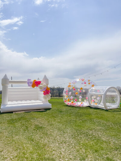 White bounce house with colorful balloons attached and a transparent bubble dome.
