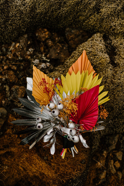 Funky silver, hot pink, yellow & orange wedding bouquet laying on mossy lava rock in Iceland!