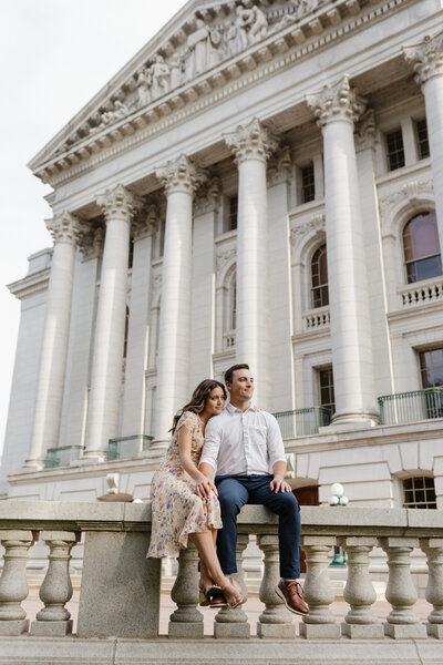 man and woman sitting on a stone wall in front of a large court house
