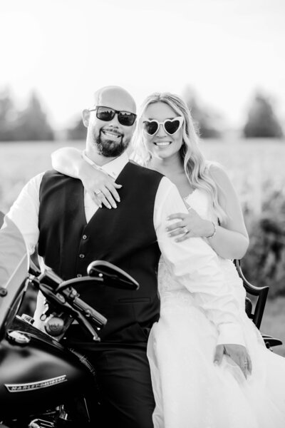 black and white photo of bride and groom sitting on motorcycle with sunglasses on