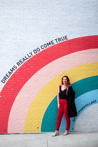 Woman standing in front of  rainbow mural with the words 'dreams really do come true'