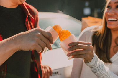 man and woman touching two hash browns together on the hood of a car