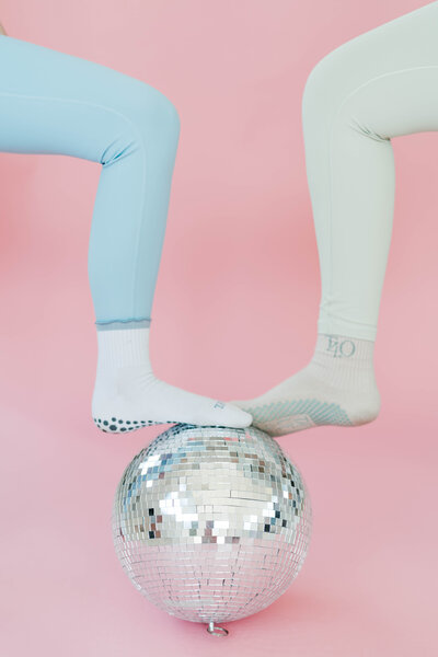 two women's feet on a disco ball with a pink background