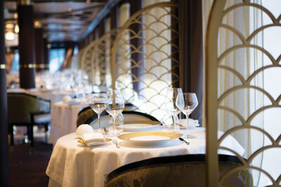 Elegant restaurant interior with white tablecloths, wine glasses, and soft lighting, separated by decorative gold partitions.