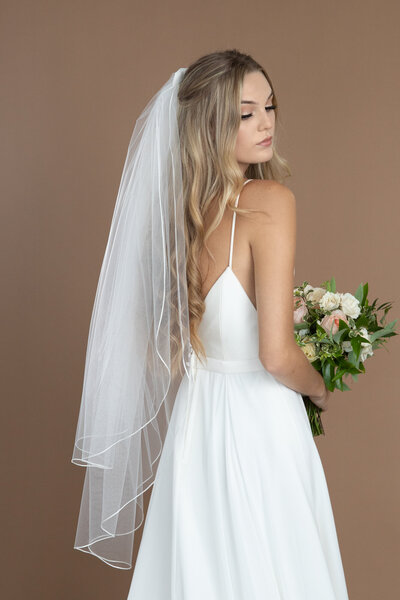 Bride wearing a two layer fingertip length veil with ribbon edge, and holding a white and blush bouquet