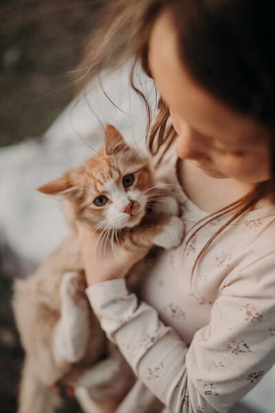  A young girl lovingly looks at her tabby cat that stares directly at the camera during a sunset session in Kiowa, Colorado.