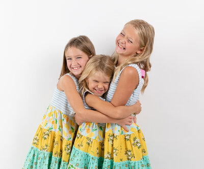 3 sisters embrace each other and giggle in matching sundresses