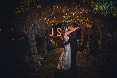 Bride and groom embracing each other under a twinkle-light-lit garden archway at Green Gables Wedding Estate wedding venue in San Marcos.