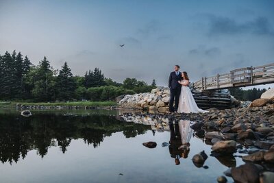 A bird flies overhead of a couple posing near calm waters on their wedding day. 