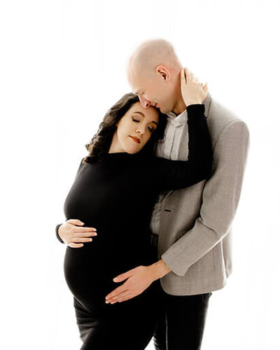 Maternity couple. Pregnant woman in black hugging a taller man in a suit jacket.
