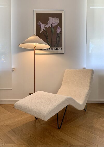 A 1951 chaise longue designed by Greta M. Grossman for Gubi, elegantly displayed in a store. A midcentury floor lamp stands beside it, with a framed artwork adorning the wall behind.