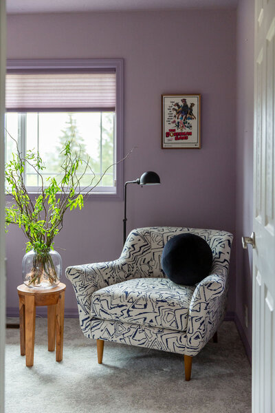 A cozy patterned chair, next to side table with house plant.
