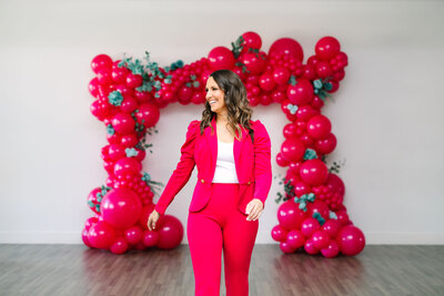 Expert in custom balloon services for luxury events wearing an elegant pink suit in front of balloon art for Raleigh Balloons, Event Décor and Rentals