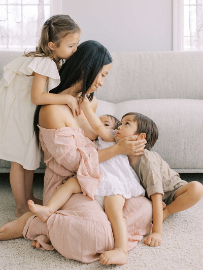 Mai with her newborn baby that is holding her hair while her big sister holds mai from the back and mai puts her hand on her son's cheek who is sitting behind the youngest.