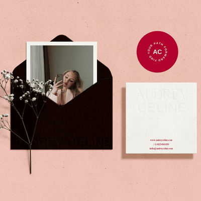 A branding mockup featuring a black envelope with a photo of Audrey Celine inside. Next to it is a white business card with embossed text and the "AC" logo. The "AC" logo is also stamped in red on a white circle with the text "Your Path Forward."