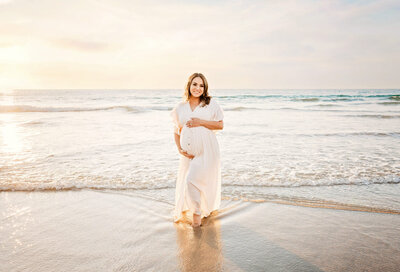 Sunset San Diego maternity photography session with a mama walking through the water holding her pregnant belly