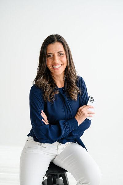 Jo founder of Branding by Jo, sitting with a cup in Orlando studio, blending professionalism with a relaxed, approachable style.o leaning against a desk at a studio in Orlando holding a white branded cup while smiling towards the camera during her own brand photo session.