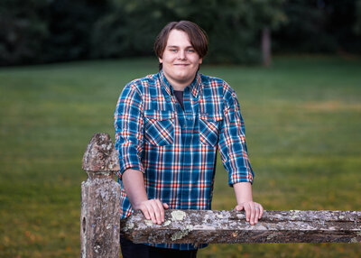 High school senior guy in plaid shirt posing in front of a fence for senior portraits in Greeley Park Nashua NH by Lisa Smith Photography