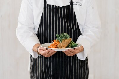 catering brand photos by Columbus photographer with chef holding a plate of food in front of his chest while wearing a black apron