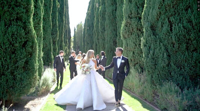 Lauren and Preston's bridal party at Beverly Hills Greystone Mansion walking down a garden path, elegantly dressed and surrounded by lush greenery and historic beauty.