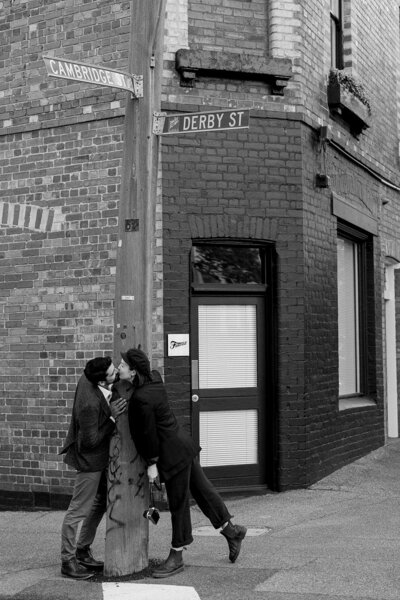 Jaz and Alejandro leaning in for a kiss, a street sign in between them
