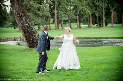 Bride and groom sharing a dance on the grass by a creek