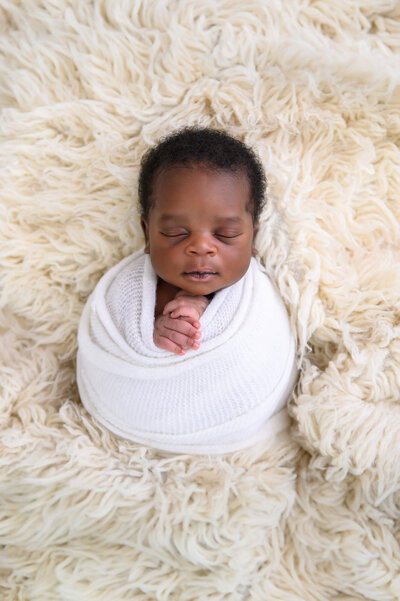 African American newborn boy wrapped in white on a cream background for his newborn photography session in Burlington, Ontario
