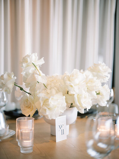 A wedding reception table adorned with lush white roses and candles, creating a soft and romantic ambiance.