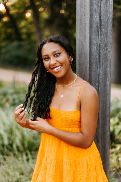 Portrait of Senior girl in an orange dress twirling her hair in her hands