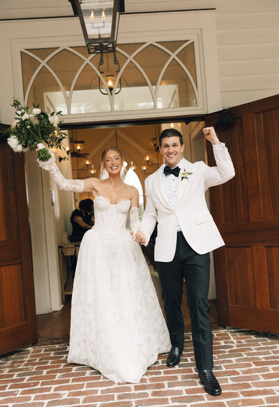 A bride and groom raise their hands while running out of the chapel in celebration of just getting married
