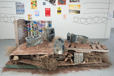 A cinder block that was hand made out of clay is decorated with underglaze to resemble graffiti and various other imagery