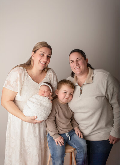 Two moms cuddle up on their two kids during a studio portrait session