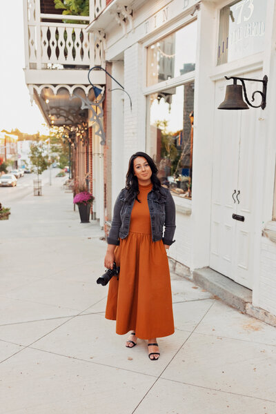 Farrah Sanjari, Ottawa mini sessions photographer, standing on a street in downtown Almonte holding a camera. 