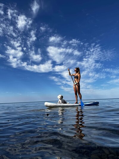 Woman practicing paddleboard yoga with her dog on a sunny day in Prince Edward County.