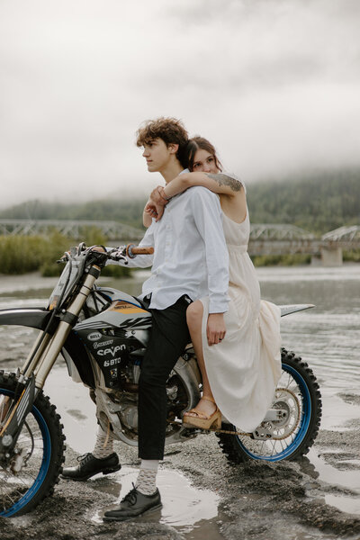 Couple on motorcycle with her arms around him by foggy Alaska river.