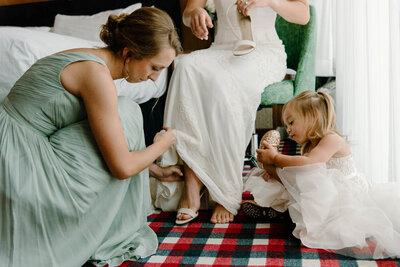 flower girl and bridesmaid helping bride put on shoes