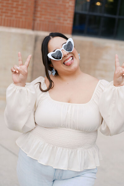 Raleigh event planner Sofia wearing white glasses holding peace signs