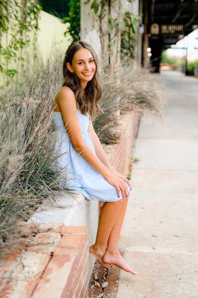 ardrey kell senior sits in a blue dress with bare feet during her grad portrait session in camp north end