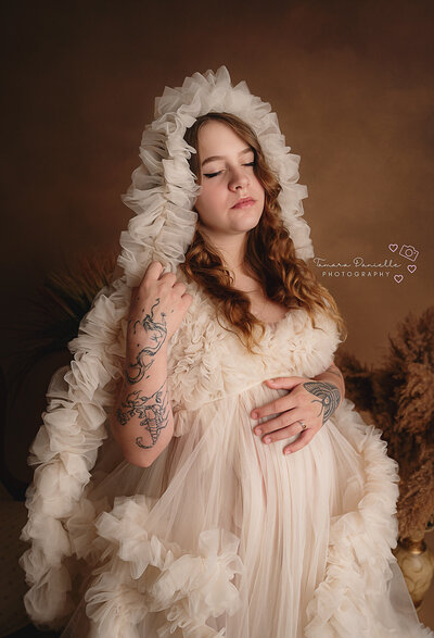 new mom wearing white gown holding newborn with floral background in studio near Niagara
