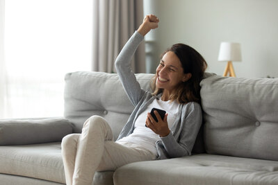 lady on a sofa with arm up in the air holding a phone in the other hand