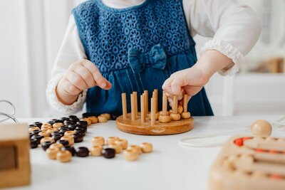 Child’s hand playing with wooden peg toys on table | educational evaluation context Rooted Within Santa Barbara