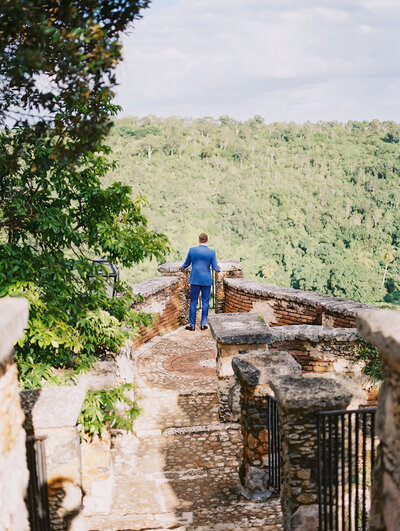 Groom walking along the stone pathways overlooking the Chavón River at Altos de Chavón — cinematic destination wedding moment captured by Asia Pimentel Photography.