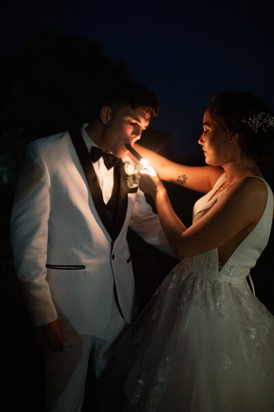 A bride and groom are lighting a cigar at their wedding reception , the glow of the cigar lights up their faced