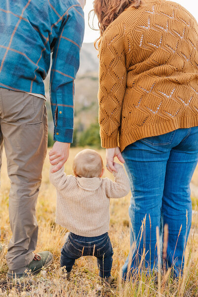 Family of 3 holding hands together at their family session in the Snowy Range Mountains near Laramie, Wyoming. 